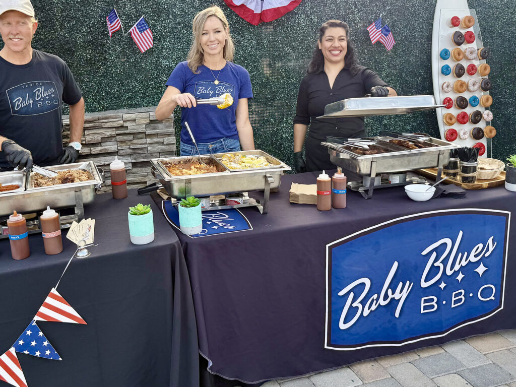 Three people serving up food from Baby Blues BBQ with Man with surfboard of donuts
