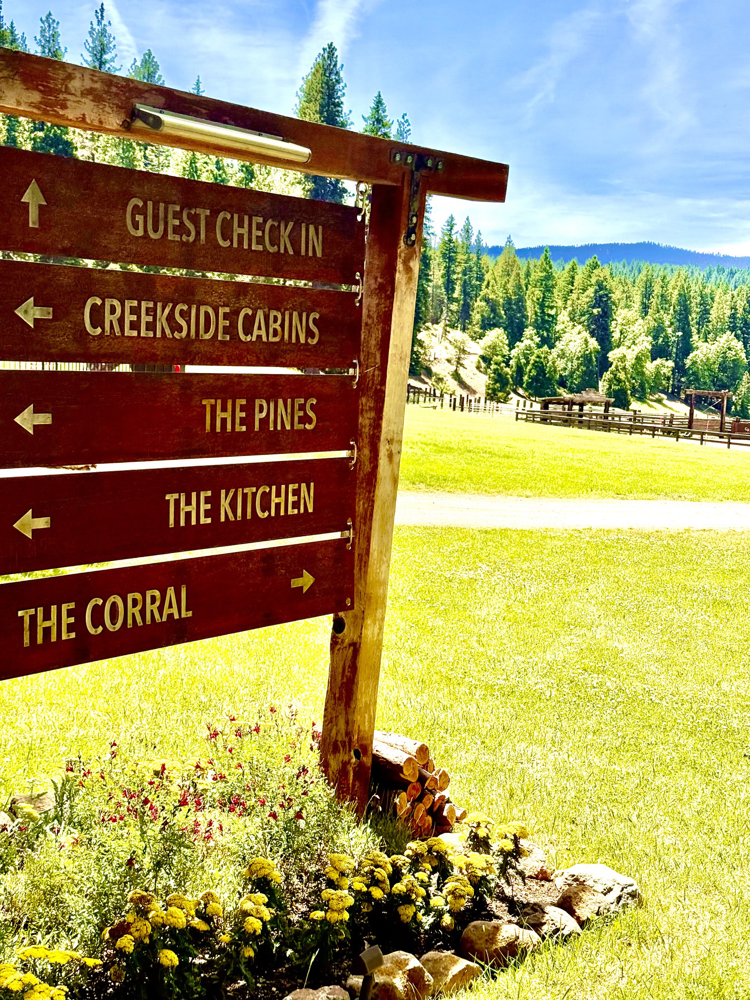 Sign with directional arrows to Guest Check In, Creekside Cabins, Pines, Kitchen and Corral