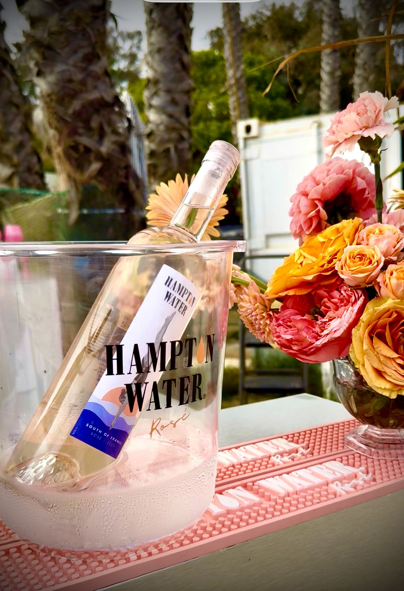 Rose and Roses Bottle of Hampton Water Rose next to a Floral Arrangement